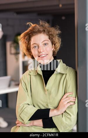 Junge lächelnde blonde Büroangestellte in Casualwear stehen Öffnen Sie die Tür Stockfoto