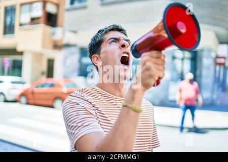 Junger hübscher kaukasischer Mann, der mit Megaphon in der Stadt schreit Stockfoto