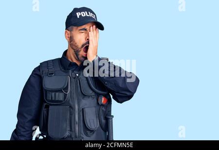 Junger hispanischer Mann mit Polizeiuniform gähnend müde, bedeckt halb Gesicht, Auge und Mund mit der Hand. Gesicht schmerzt vor Schmerzen. Stockfoto