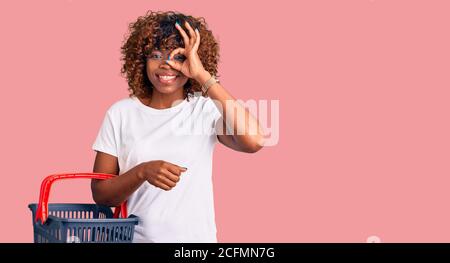 Junge afroamerikanische Frau hält Supermarkt Warenkorb lächelnd glücklich Tun ok Zeichen mit Hand auf Auge durch die Finger schauen Stockfoto