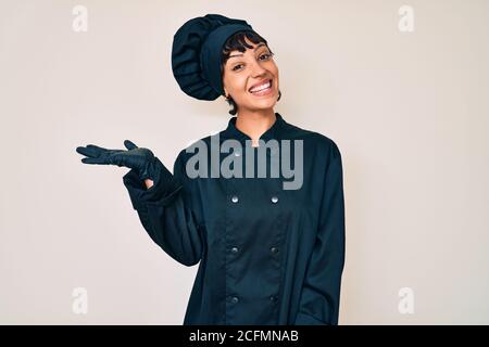 Schöne brunettte Frau trägt professionelle Koch Uniform lächelnd fröhlich präsentiert und zeigt mit Handfläche Blick auf die Kamera. Stockfoto