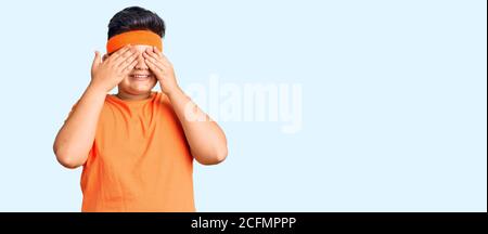 Kleiner Junge Kind trägt Sportkleidung über Augen mit Händen lächelnd fröhlich und lustig. Blind Konzept. Stockfoto