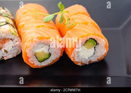 Sushi rollt philadelphia auf einem schwarzen Teller. Sushi-Brötchen-Set mit Lachs, Gemüse und Frischkäse aus der Nähe. Japanische Speisekarte Stockfoto