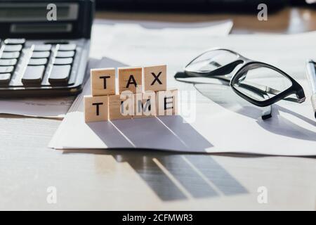 Tax Time Holzbuchstaben mit Steuerform, Brille und Rechner Stockfoto