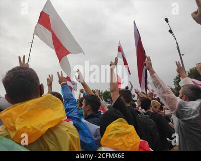 Minsk / Weißrussland - 6. September 2020: Demonstranten in bunten Regenmänteln heben die Hände mit Siegeszeichen und Fahnen in die Luft Stockfoto