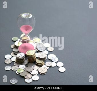 Sanduhr mit fließendem Sand und Münzen auf dem Tisch. Zeit ist Geld Konzept. Stockfoto