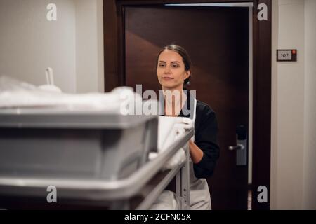 Ein energischer Haushälter schiebt einen Reinigungswagen. Stockfoto