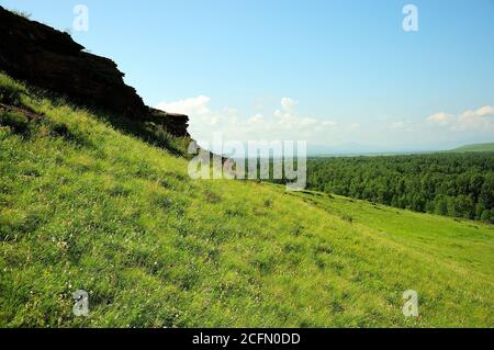 Eine alte Mauer, die entlang der Spitze eines hohen grasbewachsenen Hügel mit Blick auf ein malerisches Tal verläuft. Bergkette Truhen, Chakassien, Südsibirien, Russi Stockfoto