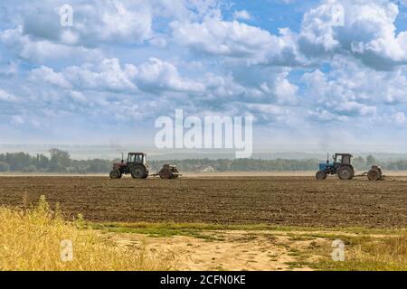 Schöne landwirtschaftliche Landschaft unter dem wolkigen Himmel - zwei alte Traktoren mit Sämaschinen ausgestattet. Bauern säen Winterweizen im Herbst Stockfoto