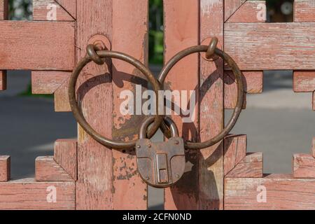 Vorhängeschloss und Metallringe an verwitterten alten Holztoren. Vintage, rostig und geschlossen alten Schließsystem. Stockfoto