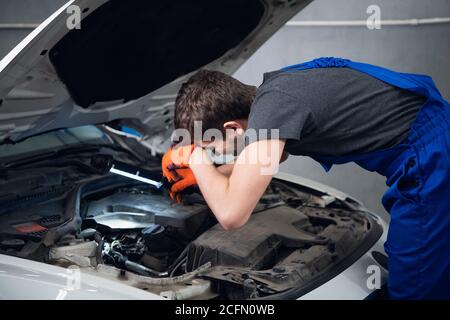 Ein Mann in Overalls inspiziert einen Automotor mit einem Lampe Stockfoto