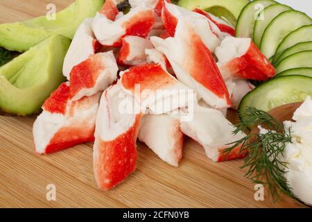 Krabbenstäbchen schneiden Fleisch und Gemüse Avocado schneiden Gurken auf Holzschneidebrett aus nächster Nähe Stockfoto