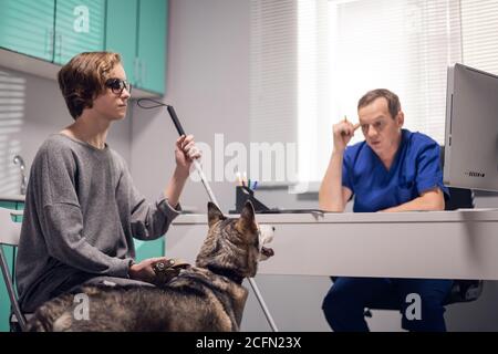 Ein blindes Mädchen mit einem Blindenhund bittet um professionellen Rat von einem Tierarzt. Stockfoto
