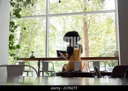 Junge afrikanische Frau Student mit Laptop halten Telefon sitzen am Café-Tisch. Stockfoto