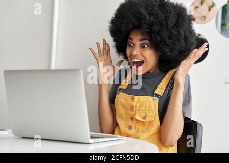 Aufgeregt afrikanische Frau Blick auf Laptop gewinnen online, lesen gute Nachrichten. Stockfoto