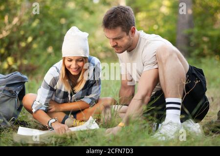Junge Wanderer sitzen auf dem Boden und betrachten eine alte Karte mit einem Kompass. Wanderpaar in der Natur. Stockfoto