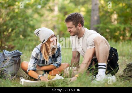 Junge Wanderer sitzen auf dem Boden und betrachten eine alte Karte mit einem Kompass. Wanderpaar in der Natur. Stockfoto