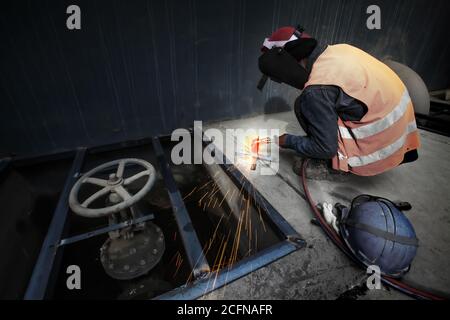 Asiatischer Mann schweißen ein Metallrost, Lichtbogenschweißprozess mit Funken. Langzeitbelichtung. Konzentrieren Sie sich auf funkelnde. Stockfoto