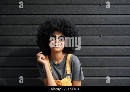 Glücklich lustige afrikanische Hipster Frau tragen stilvolle Sonnenbrille gegen schwarze Wand. Stockfoto