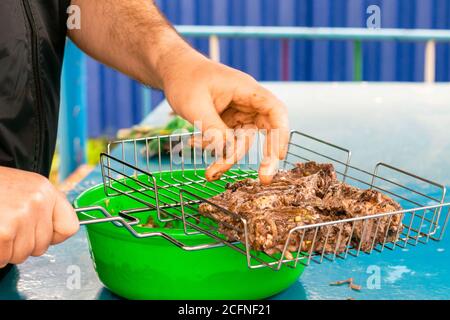 Mann legt mariniertes Grillfleisch auf den Grill im Gartenpavillon Stockfoto