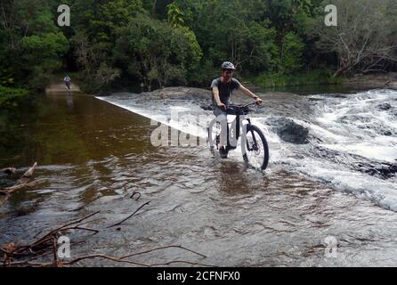 Mann fährt mit dem Elektrofahrrad über den Damm am Little Mulgrave River, Goldfield Trail, Goldsborough Valley, nahe Cairns, Queensland, Australien. Nein, MR Stockfoto