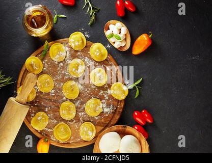 Leckere Ravioli mit Mehl, Kirschtomaten, Sonnenblumenöl und Basilikum auf dunklem Grund. Der Prozess der Herstellung von italienischen Ravioli. Speicherplatz kopieren. Flach l Stockfoto