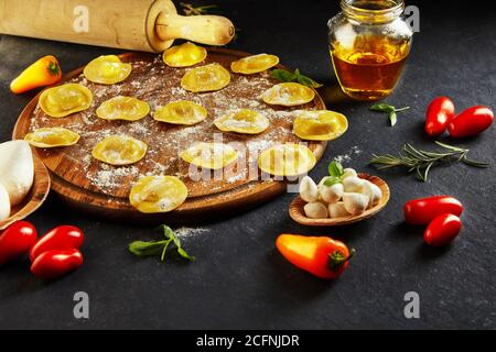 Leckere Ravioli mit Mehl, Kirschtomaten, Sonnenblumenöl und Basilikum auf dunklem Grund. Der Prozess der Herstellung von italienischen Ravioli. Seitenansicht. Stockfoto