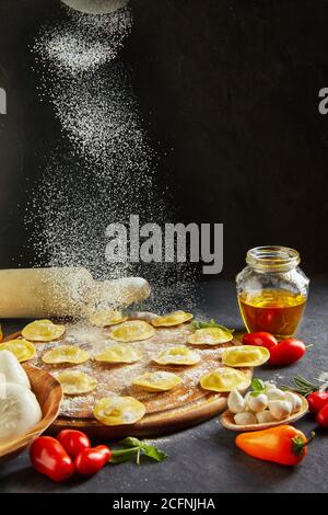 Köstliche rohe Ravioli mit Käse und Mehl, Kirschtomaten, Sonnenblumenöl und Basilikum auf dunklem Grund. Der Prozess der Blüte der italienischen Raviol Stockfoto