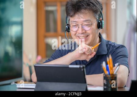 Asiatischer Mann mittleren Alters, der zu Hause arbeitet. Telearbeitkonzept. Stockfoto