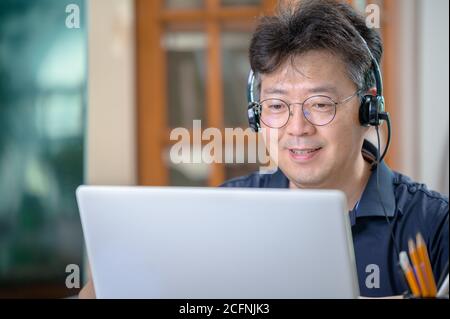 Asiatischer Mann mittleren Alters, der zu Hause arbeitet. Telearbeitkonzept. Stockfoto