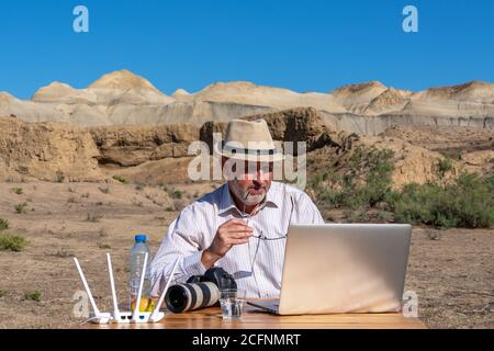 Fotograf im Hut arbeitet am Tisch im Freien auf Laptop Stockfoto