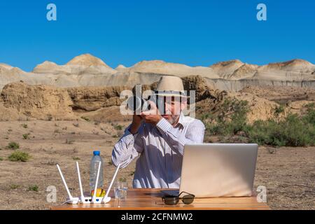 Fotograf im Hut arbeitet am Tisch im Freien auf Laptop Stockfoto
