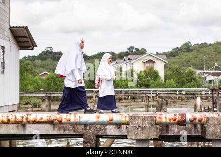 Bandar Seri Begawan / Brunei - 16. Januar 2019: Muslimische Mädchen in weißer muslimischer Schuluniform gehen durch Holzwege im schwimmenden Dorf Kampong Ayer zur Schule Stockfoto