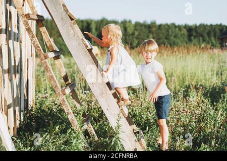 Nette Geschwister kleines Mädchen und junge Bruder Schwester klettert nach oben Die Leiter Landschaft cottagecor Stockfoto