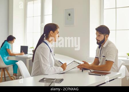 Medizinische Klinik. Lächelnde Frau Arzt sitzen und hören zu reden Mann Patient während der Konsultation Stockfoto