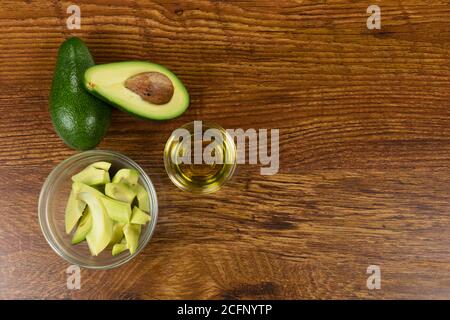 Blick auf zwei Avocados, Olivenöl-Flasche und Schnitt Avocado in einer Schüssel auf Holztisch Hintergrund Stockfoto