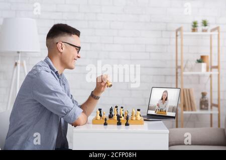 Online-Meeting und Hobby in Selbstisolation. Guy spielt zu Hause Schach und schaut sich den Laptop an Stockfoto