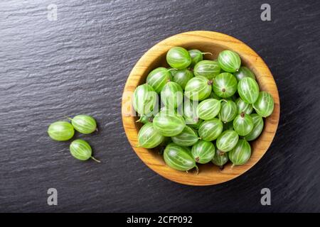 Frische Stachelbeeren in Holzschale auf schwarzem Stein Schiefer Hintergrund. Draufsicht. Stockfoto