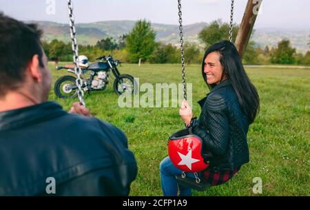 Glückliche junge Frau, die ihren Freund auf einem sitzend Schaukel Stockfoto