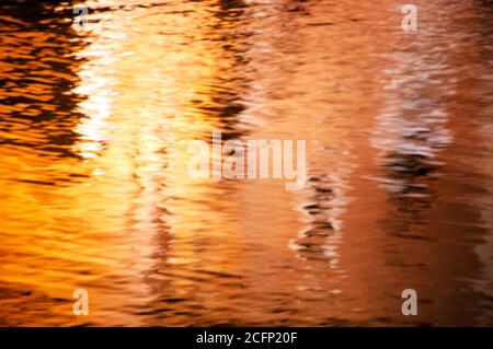 Verschwommenes Spiegelbild von bunten Häusern (beleuchtet von Straßenlaternen) im Kanalwasser in der Nacht. Venedig, Italien. Abstrakter Hintergrund. Stockfoto
