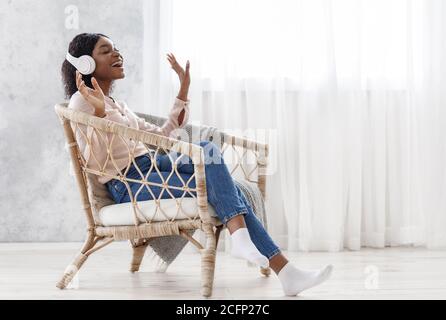 Carefree Black Girl Musik Hören In Kabellose Kopfhörer Und Singen Zu Hause Stockfoto