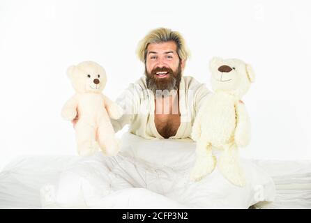 Gute Stimmung. Verspielt und romantisch. Mann umarmt Spielzeug entspannen im Bett. Imaginäre Freunde. Bemühen Sie sich, gute Schlafgewohnheiten zu üben. Niedliche Teddybär Spielzeug. Positive Schlafzimmerumgebung. Bärtige Hipster spielen Spielzeug. Stockfoto