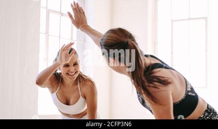 Lächelnde Fitness-Frauen heben die Hände, um eine hohe fünf während des Trainings zu geben. Fröhliche sportliche Frauen genießen das Fitnesstraining in einem Fitnessstudio. Stockfoto