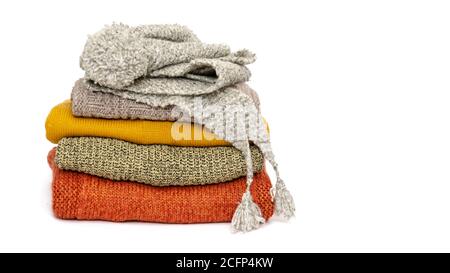 Ein Stapel gefaltetes Strickpullover, Schal und Mütze auf weißem Hintergrund. Zeit zum Warmhalten. Saison der warmen Kleidung. Nahaufnahme. Speicherplatz kopieren Stockfoto