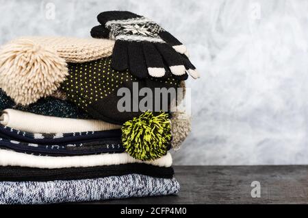 Ein Stapel von ordentlich gefalteten gestrickten Winterschals, Hüten mit Pompons und Handschuhen auf grauem Hintergrund. Saison der warmen Kleidung. Zeit zum Warmhalten. Nahaufnahme Stockfoto