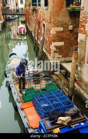 VENEDIG, ITALIEN - 14. FEBRUAR 2015: Ein Mann, der Getränke an die lokalen Pubs und Restaurants verteilt, entlädt Bierkegs und Flaschen von seinem Boot und Uplo Stockfoto