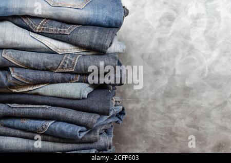 Ein Stapel achtlos gefalteter Jeans auf grauem Hintergrund. Nahaufnahme von Jeans in verschiedenen Farben. Jeans-Struktur oder Denim-Hintergrund. Speicherplatz kopieren Stockfoto