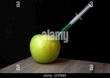 Grüner Apfel auf einem Holzbrett und Spritze darin Extraktion grüne Flüssigkeit Stockfoto