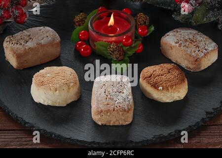 Polvorone und entzündete dekorative rote Kerze auf runder Schieferplatte.Polvoron Ist ein typisches Produkt von Weihnachtsgebäck in Spanien Stockfoto
