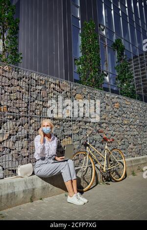Stilvolle Frau in Schutzmaske sprechen auf Handy in Im Freien Stockfoto